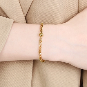 Detail eines goldenen Figaro-Kettenarmbands mit Kugeldekor am Handgelenk des Models