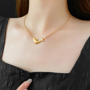Close-up of minimalist gold whale necklace with small zircon pendant worn by a model