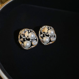 Close-up of silver earrings with irregular hollow frames, pearls, and sparkling rhinestones