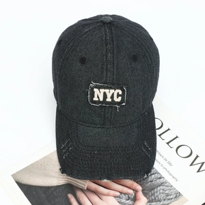 Detailed close-up of distressed denim baseball cap with NYC embroidery and frayed edges
