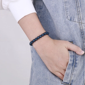Detail of 8mm blue agate beads bracelet worn on hand against denim fabric texture