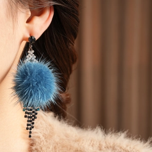 Detail of model wearing blue pom-pom earrings with sparkling long rhinestone tassels
