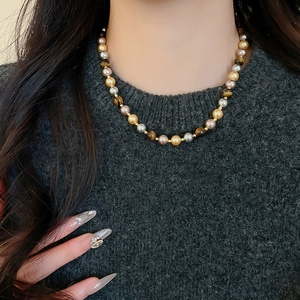 Détail d'un collier vintage français en œil de tigre et perles sur un mannequin en gris