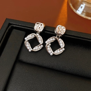 Detailed view of silver-plated square pearl earrings with hollow texture on a display stand
