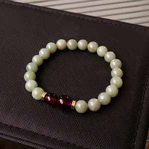 Detail view of light green Hetian jade beads with dark red accents on dark background