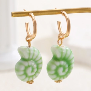 Gros plan de créoles dorées avec pendentifs nautiles en céramique blanche et verte