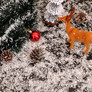 Flat lay of artificial snow with reindeer, pine branches, and red Christmas ornaments