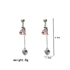 Détail de boucles d'oreilles pendantes argentées avec cœurs en cristal rose et dauphins
