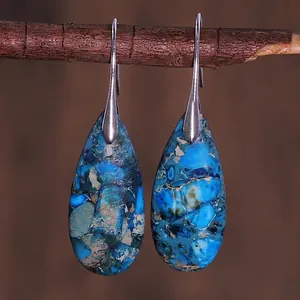 Detail of teardrop emperor stone earrings with blue texture hanging on wooden branch