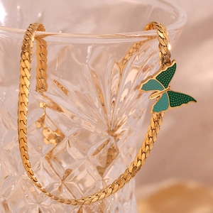 Close-up of 18K gold-plated NK chain featuring a green butterfly pendant on a crystal glass