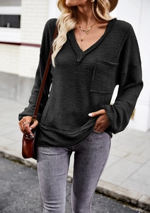 Outdoor street view of a black waffle knit hooded sweater with a large front pocket