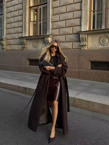 Photo street style d'une femme en trench-coat marron long avec une jupe en cuir assortie