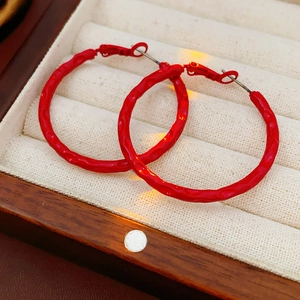 Macro shot of red round hoop earrings with textured finish on beige velvet display