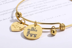 Detail of gold titanium steel bracelet with mama charm and heart pendant on paper