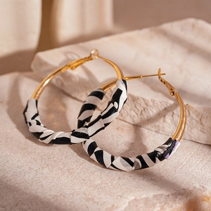 Detail view of gold hoop earrings with black and white striped texture on stone surface