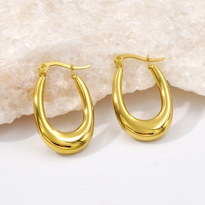 Detailed close-up of golden U-shaped oval hoop earrings on a textured stone surface