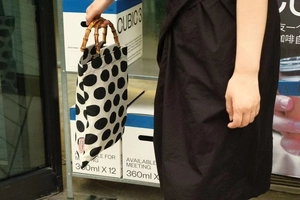 Detail of canvas handbag featuring bold black polka dots and a natural bamboo handle