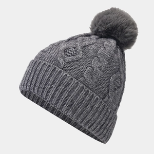 Close-up of a dark grey knit beanie with classic cable pattern and a faux fur pom-pom
