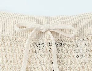 Detail of beige crochet knit fabric showing drawstring waist and openwork texture