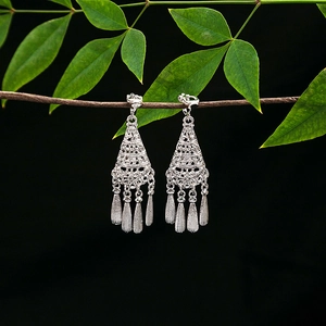 Close-up of silver tassel earrings with hollow patterns on a green leaf branch