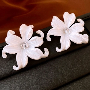 Elegant white lily acrylic flower earrings with sparkling central zircon on silk background
