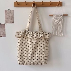 Detailed close-up of polka dot canvas tote bag with ruffled trim and brand woven label