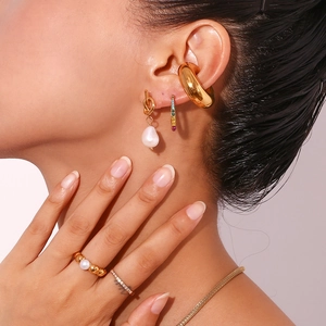 Close-up of stacked gold knot earrings with freshwater pearls and zircon accents