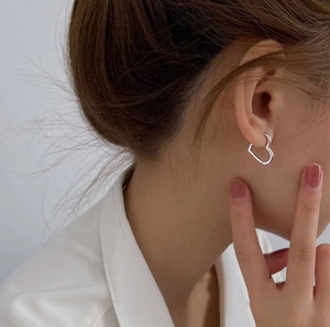 Elegant hollow heart-shaped silver hoop earrings worn by a model in a close-up profile shot