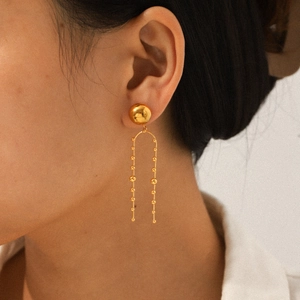 Elegant gold stainless steel U-shaped drop earrings with bead tassels worn by a model
