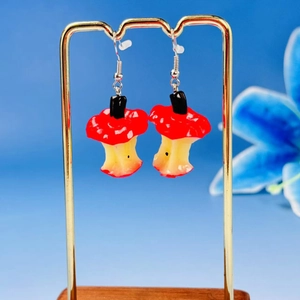 Macro detail of red apple core earrings with cute festive design and gold metal hooks