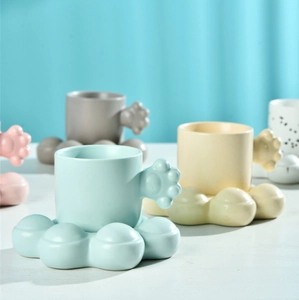 Close-up of ceramic coffee mug featuring a thick cat-paw handle and matching coaster