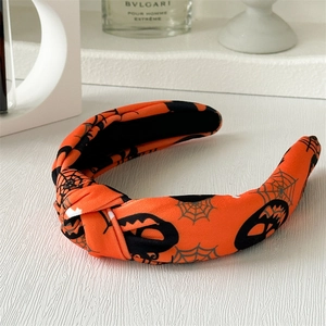 Détail d'un serre-tête noué en tissu orange avec motifs de citrouilles et toiles d'araignées