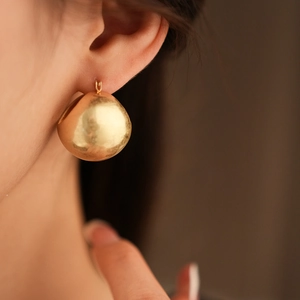 Close-up of a large polished gold circular basket earring worn by a model in soft light