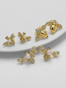 Detalle macro de pendientes de abeja chapados en oro con circonitas y perlas