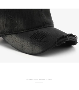 Detailed close-up of distressed brim on black cotton baseball cap with vintage frayed edges