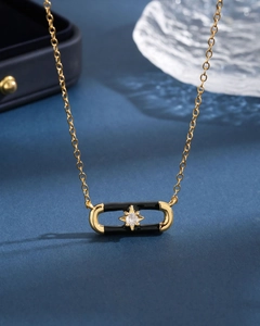 Detail view of a gold pendant necklace featuring black enamel and a star-set white zircon