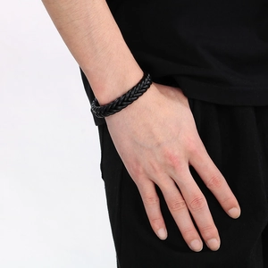 Detail of a braided black leather bracelet with stainless steel clasp on a male wrist