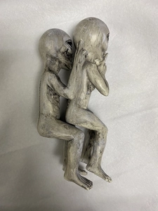 Macro detail of two grey resin alien figurines positioned on a textured grey paper surface
