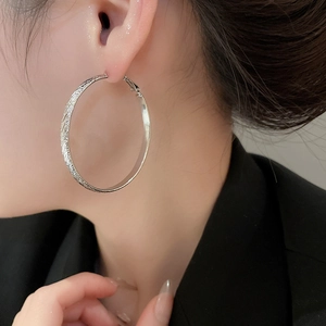 Close-up of a silver textured hoop earring worn by a model in a minimalist style