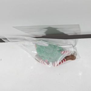 Detail of green plush Christmas tree doll with red striped legs in protective packaging