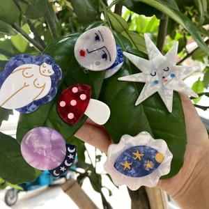 Detail of whimsical acetate hair clips with mushroom, star and face designs on green leaves