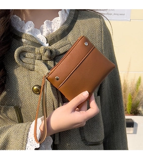 Brown leather coin purse with lychee texture and wristlet held by a model in a retro coat