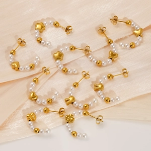 Gold C-shaped pearl earrings with heart and star charms on beige silk fabric