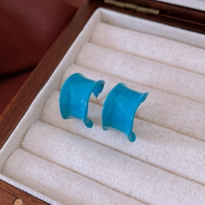 Détail des boucles d'oreilles courbées en émail bleu sarcelle sur écrin en bois blanc
