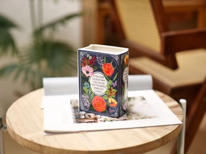 Artistic book-shaped ceramic vase with floral patterns and garden quotes on a wooden table