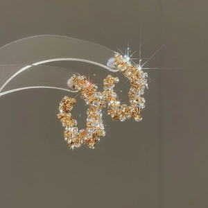Macro shot of gold C-shaped earrings with shimmering rhinestones and white pearls