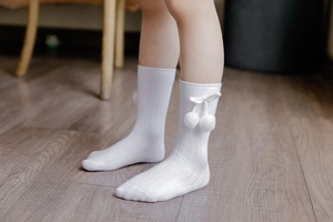 Close-up of white ribbed knee-high baby socks with plush pom-pom bow detail