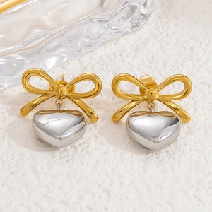 Detail of gold bow earrings with silver heart pendants on white textured background