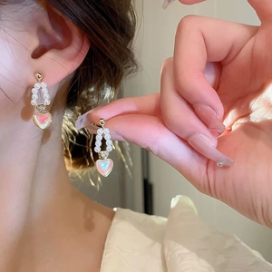 Detailed close-up of heart-shaped pearl drop earrings on model with golden accents