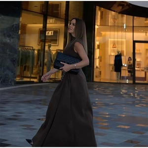 Outdoor street view of a woman wearing a dark brown sleeveless maxi dress with a high neck